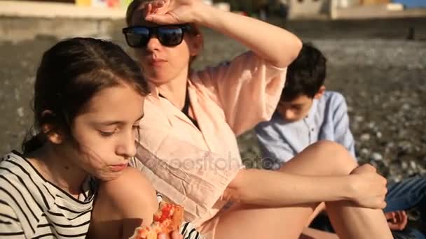 Діти з матір'ю їдять піцу на пляжі — стокове відео