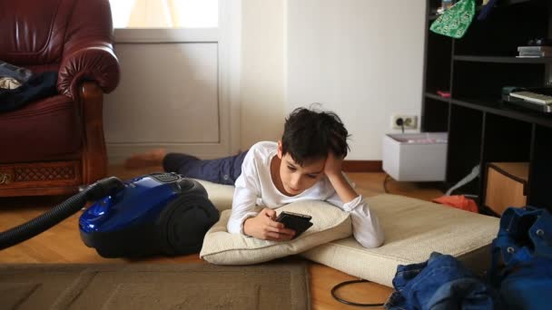 Rapaz adolescente está fugindo de seu dever de casa, jogando em seu telefone celular. Limpeza do quarto das crianças. Transtorno no quarto adolescente — Vídeo de Stock