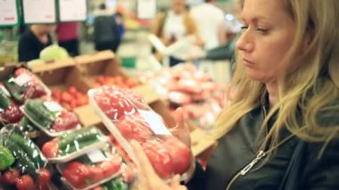 Bir kadın bir sebze rafta bir süpermarkette sebze ve meyve satın alır. Domates adam seçer