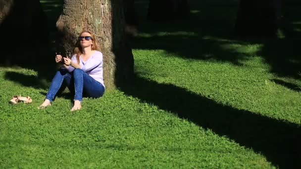 Mujer guapa sentada debajo de una palmera y navegando por Internet en un smartphone — Vídeo de stock