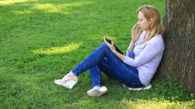 Bir palmiye ağacının altında oturan ve browsing belgili tanımlık enterne üstünde bir smartphone yakışıklı kadın