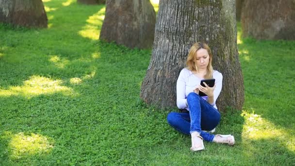 Knappe vrouw zittend onder een palmboom en surfen op het Internet op een smartphone — Stockvideo