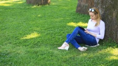 Bir palmiye ağacının altında oturan ve browsing belgili tanımlık enterne üstünde bir smartphone yakışıklı kadın