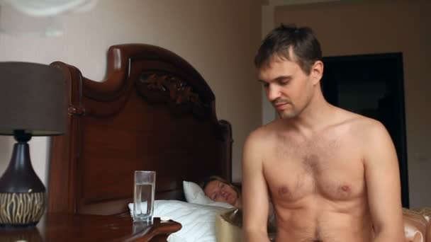 Чоловік приймає таблетку перед сексом. Жінка чекає чоловіка в ліжку — стокове відео