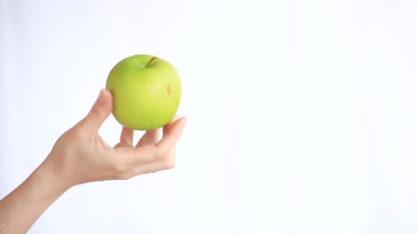 La mano femenina sostiene una manzana verde sobre un fondo blanco — Vídeos de Stock