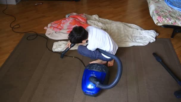 El chico limpia la alfombra en la habitación con una aspiradora — Vídeos de Stock