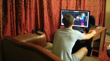 Bir T-shirt ve şort, evde koltukta oturan bir adam Döviz Alım Satım, zamanında değişimler bilgisayar monitörü seyir izler