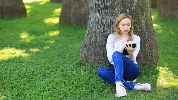 Όμορφος γυναίκα κάθεται κάτω από ένα φοίνικα και περιήγηση στο Internet σε ένα smartphone — Αρχείο Βίντεο