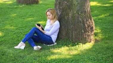 Bir palmiye ağacının altında oturan ve browsing belgili tanımlık enterne üstünde bir smartphone yakışıklı kadın