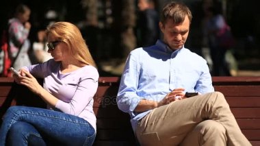 Erkek ve kadın bir bankta oturan farklı yönlere bakıyor. Herkes onun cep telefonu bakıyor