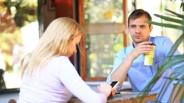 Verliebtes Paar in einem Café im Freien. Mann und schöne Frau bei einem Date. Jeder schaut auf sein Handy — Stockvideo