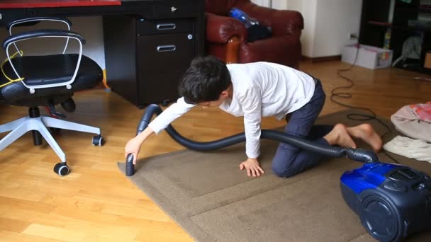 Мальчик чистит ковер в комнате пылесосом — стоковое видео