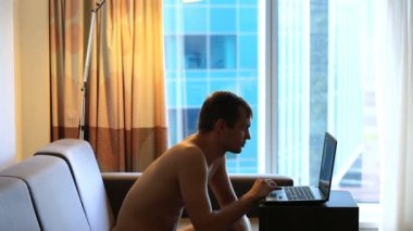 Adam kanepede büyük pencerenin önünde oturan dizüstü bilgisayarda yazarak