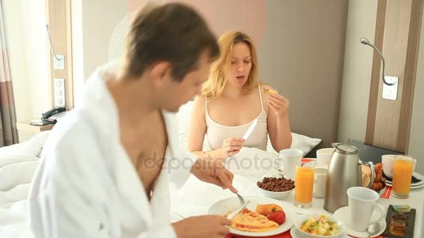 Pareja joven hombre y mujer desayunando en la cama en el apartamento — Vídeo de stock