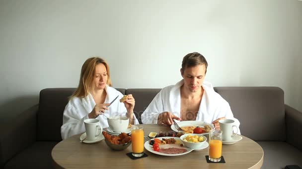 Mladý pár, muž a žena mají snídani na pohovce v hotelovém pokoji — Stock video