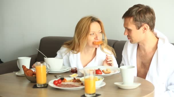Mladý pár, muž a žena mají snídani na pohovce v hotelovém pokoji — Stock video