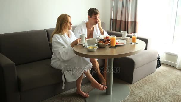 Jeune couple homme et femme petit déjeuner sur canapé dans la chambre d'hôtel — Video