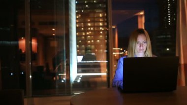 Güzel sarışın iş kadını fazla mesai çalışma gece çift ofisinde. Şehir ışıkları arka plan büyük bir pencere görünür