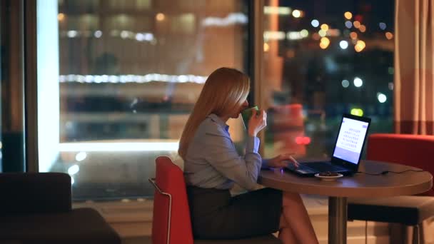 Krásná blondýna obchodní žena pracující přesčas v noci v kabinet. Město světla jsou vidět v pozadí z velkého okna — Stock video