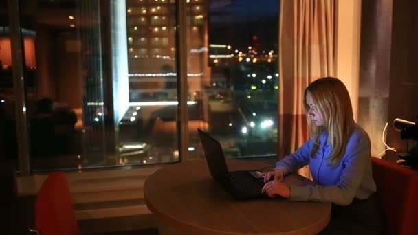 Mulher de negócios loira bonita trabalhando horas extras à noite no escritório executivo. Luzes da cidade são visíveis no fundo de uma grande janela — Vídeo de Stock