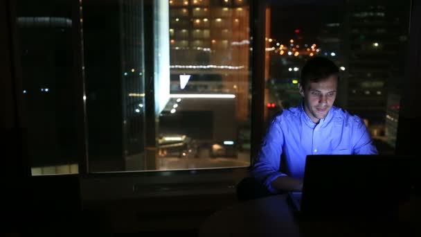 Hermoso hombre de negocios trabajando horas extras por la noche en la oficina ejecutiva. Las luces de la ciudad son visibles en el fondo desde una ventana grande — Vídeos de Stock