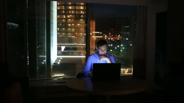 Hermoso hombre de negocios trabajando horas extras por la noche en la oficina ejecutiva. Las luces de la ciudad son visibles en el fondo desde una ventana grande — Vídeo de stock