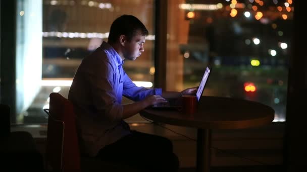 Hermoso hombre de negocios trabajando horas extras por la noche en la oficina ejecutiva. Las luces de la ciudad son visibles en el fondo desde una ventana grande — Vídeos de Stock