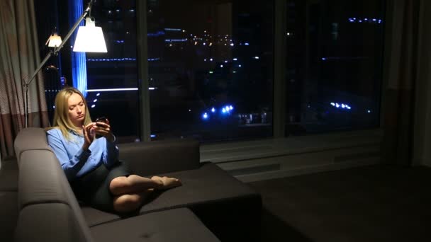 Деловая женщина, блондинка, просматривающая интернет по телефону. В реальном времени. Панорамное окно и ночной город на заднем плане . — стоковое видео