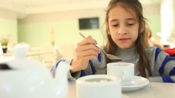 Un niño bebe té caliente con una cuchara en un café — Vídeo de stock