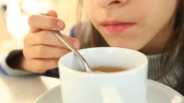 Un enfant boit du thé chaud avec une cuillère dans un café — Video
