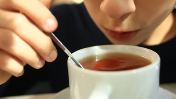 Uma criança bebe chá quente com uma colher em um café — Vídeo de Stock