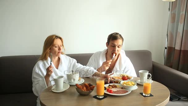 Pareja joven hombre y mujer desayunando en el sofá en la habitación de hotel — Vídeos de Stock
