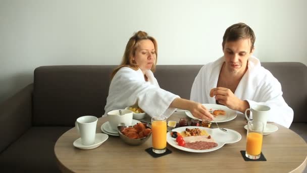 Young couple man and woman having breakfast on sofa in hotel room — Stock Video