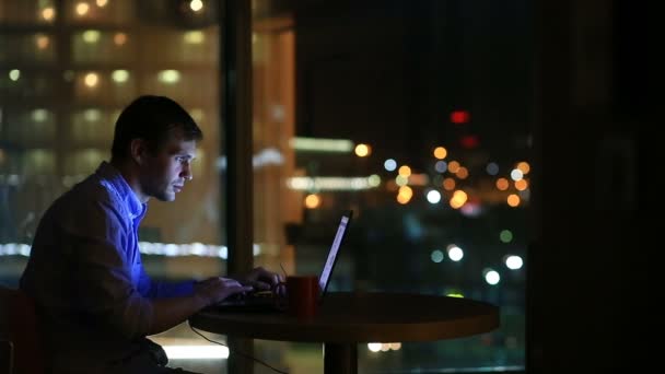 Hermoso hombre de negocios trabajando horas extras por la noche en la oficina ejecutiva. Las luces de la ciudad son visibles en el fondo desde una ventana grande — Vídeos de Stock