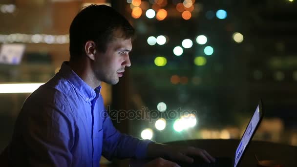 Hermoso hombre de negocios trabajando horas extras por la noche en la oficina ejecutiva. Las luces de la ciudad son visibles en el fondo desde una ventana grande — Vídeo de stock