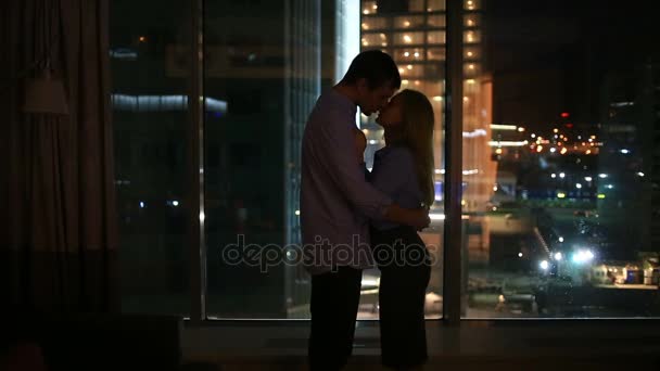 Ένα ζευγάρι των ανδρών και των γυναικών που αναζητούν σε ένα μεγάλο παράθυρο σε μια πόλη το βράδυ. αγκαλιά — Αρχείο Βίντεο