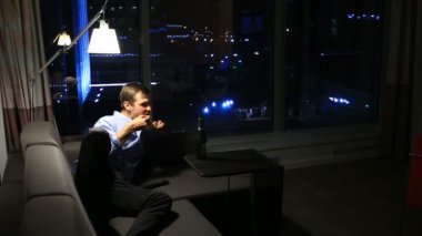 Adam kanepede geceleri evde istirahat, bira içme ve tarassut Tv, gece şehir manzaralı bir büyük ponamramnogo pencere arka planı