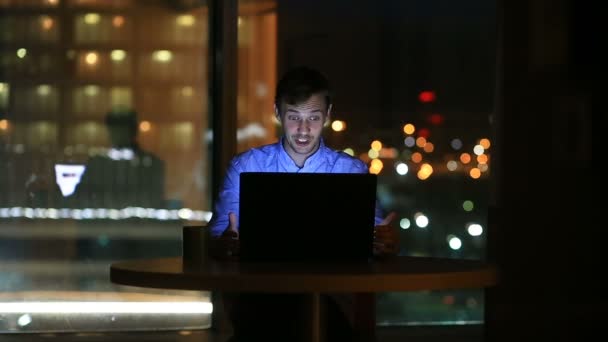 Hermoso hombre de negocios trabajando horas extras por la noche en la oficina ejecutiva. Las luces de la ciudad son visibles en el fondo desde una ventana grande — Vídeos de Stock