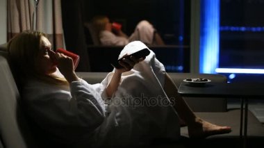 Bir kadın onun ellerinde pencere ile bir gece kenti yakınındaki bir kupa ile kanepede yatıyor. Tv izleme