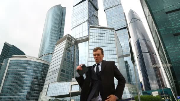 Empresário feliz dança em uma rua da cidade contra o pano de fundo de um arranha-céu de centro de negócios — Vídeo de Stock