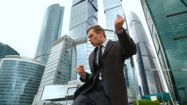 Glad affärsman danser på en stadsgata mot bakgrund av en business center skyskrapa — Stockvideo