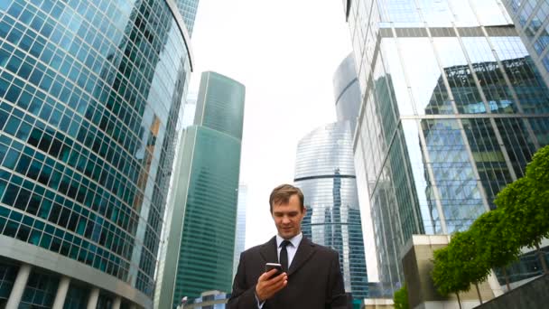 Zakenman in de stad maken van een telefoongesprek met smartphone. Tegen de achtergrond van wolkenkrabbers — Stockvideo