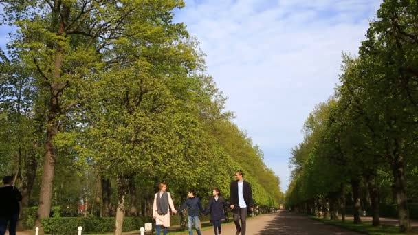 Glückliche Familie, die an einem sonnigen Tag in Mänteln und Jacken in einem Park spazieren geht — Stockvideo