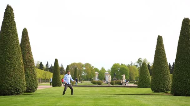 Смішний молодий білий чоловік танцює на зеленому газоні в парку в літній сонячний день — стокове відео