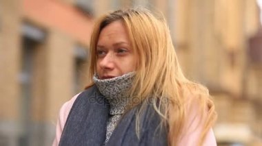 Bir pembe ceket ve kazak yorgun bir kadın kalabalık bir sokak ortasında duruyor ve soğuktan küçülür