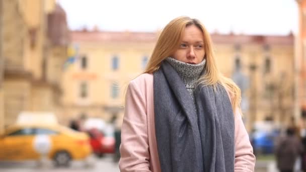 En trött kvinna i en rosa kappa och tröja står mitt i en trång gata och krymper från kylan — Stockvideo