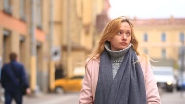 Bir pembe ceket ve kazak yorgun bir kadın kalabalık bir sokak ortasında duruyor ve soğuktan küçülür