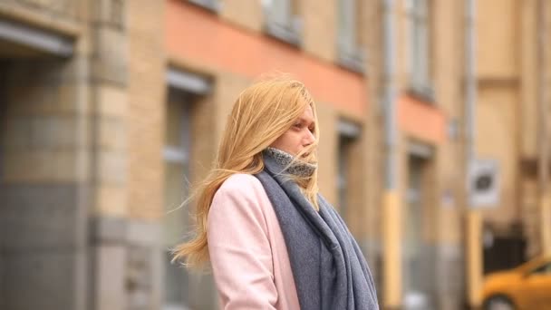 Una donna stanca in un cappotto rosa e maglione si trova in mezzo a una strada affollata e si restringe dal freddo — Video Stock