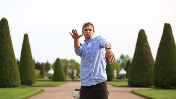 Смішний молодий білий чоловік танцює на зеленому газоні в парку в літній сонячний день — стокове відео
