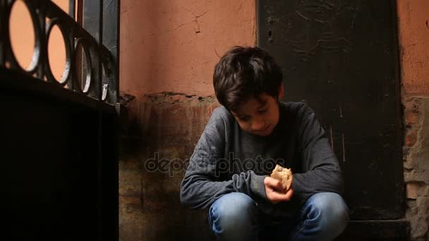 Бездомный подросток ест корочку хлеба в воротах на фоне решетки — стоковое видео